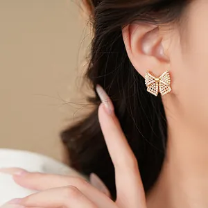 Detailansicht eleganter goldener Schleifenohrringe mit Perlen und Kristallen am Ohr des Models