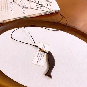 Detailweergave van een houten vis hanger aan een zwarte koordketting in een rustiek dienblad.