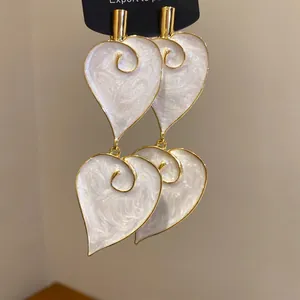 Nahaufnahme eleganter Herz-Ohrhänger mit weißem Perlmutt-Emaille und goldener Verzierung