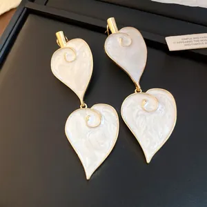 Elegante goldene Hängeohrringe mit herzförmigen Emaille-Details in weißer Marmoroptik