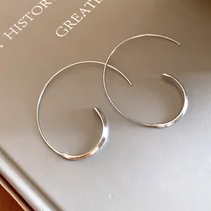 Nahaufnahme minimalistischer silberner C-förmiger Creolen auf einem eleganten Buchcover