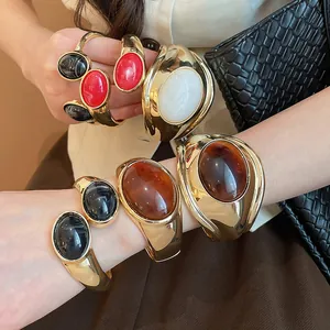 Dettaglio di grandi bracciali aperti in resina ovale con elegante finitura dorata