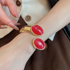 Vista dettagliata di un elegante bracciale aperto dorato con due grandi pietre in resina rossa