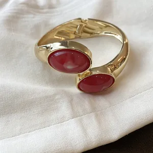 Elegante bracciale rigido dorato con due pietre ovali in resina rossa su stoffa