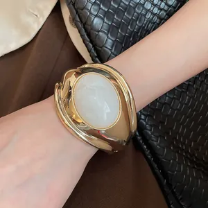Dettaglio di un bracciale a polsino dorato con una grande pietra ovale in resina bianca
