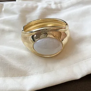 Dettaglio di un bracciale a polsino dorato con un intarsio ovale in resina bianca