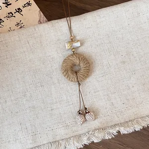 Close-up of a rustic woven jute pendant and shell-shaped charms on a linen background