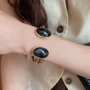 Primo piano di un bracciale aperto ovale in resina nera marmorizzata con finitura oro