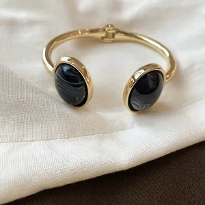 Dettaglio ravvicinato di un bracciale rigido dorato con resina nera effetto marmo
