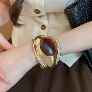 Dettaglio di bracciale rigido dorato con grande pietra ovale in resina marrone al polso