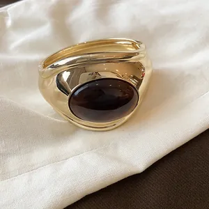 Primo piano di un lussuoso bracciale rigido dorato con resina ovale marrone scuro