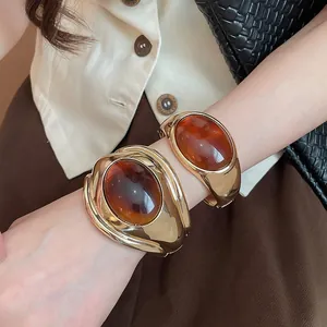 Dettaglio di bracciali rigidi dorati vintage con grandi pietre in resina ambrata.