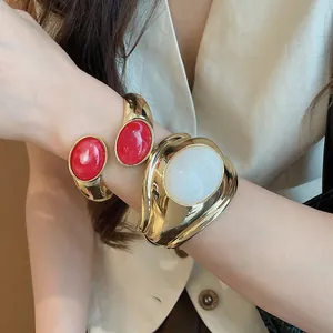 Primo piano di bracciali a polsino dorati con inserti in resina rossa e bianca al polso