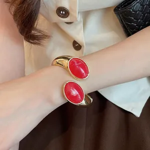 Primo piano dettagliato di un elegante bracciale aperto dorato con pietre ovali in resina rossa