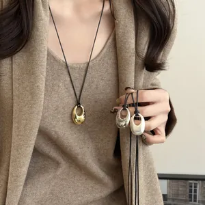 Detailansicht minimalistischer ovaler Anhänger an schwarzen Lederkordeln in Gold und Silber