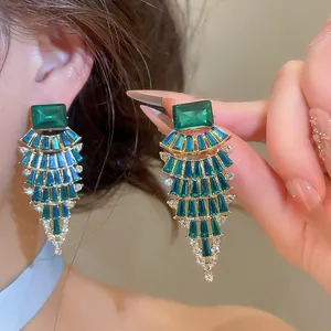 Close-up detail of emerald green fan-shaped crystal chandelier earrings with gold finish