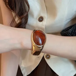 Dettaglio della pietra in resina ambrata su un elegante bracciale a fascia aperta oro.