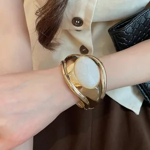 Vista dettagliata di un ampio bracciale rigido dorato con resina bianca ovale lucida