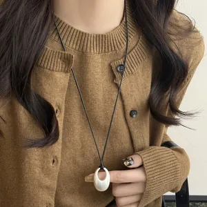 Minimalist oval silver pendant necklace on black leather cord, chic sweater chain