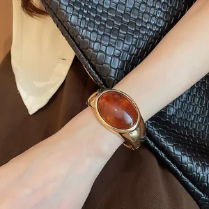 Dettaglio di un elegante bracciale a polsino dorato con una grande pietra ovale in resina.