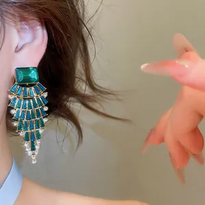Detail view of elegant large green fan-shaped rhinestone drop earrings on a model