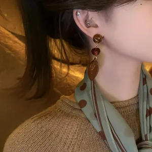 Close-up of Maillard style amber resin earrings worn by a model in warm ambient light.