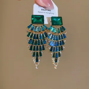 Close-up of fan-shaped dangle earrings with emerald crystals and gold-tone finish