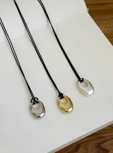 Minimalistische Halskette mit ovalem Anhänger und schwarzer Lederschnur, in drei Metallfarben.