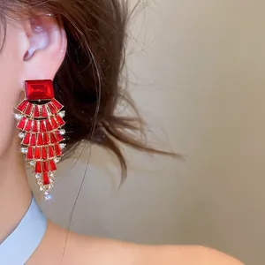 Close-up detail of luxurious red rhinestone fan-shaped drop earrings worn by a model