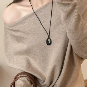 Nahaufnahme einer minimalistischen schwarzen ovalen Halskette auf einem beigen Strickpullover