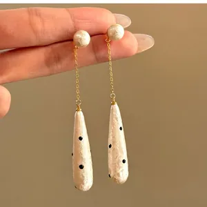 Detailed view of vintage polka dot teardrop earrings with pearl studs and gold chain.
