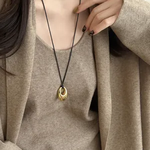 Detailansicht eines goldenen elliptischen Anhängers an einer schwarzen Kordelkette