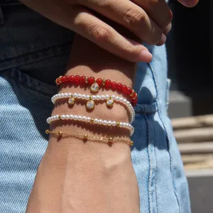 Détail de bracelets superposés dorés avec de l'agate rouge, des perles et des zircons