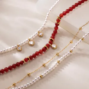 Détail rapproché de bracelets rétro avec agate rouge, perles blanches et chaînes dorées.