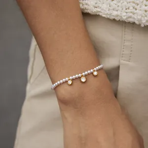 Gros plan d'un bracelet en perles avec trois breloques en zircone bordées d'or au poignet.