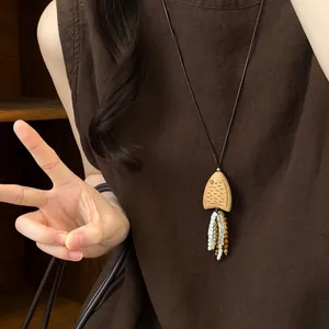 Détail d'un collier pendentif poisson en bois fait main porté sur une robe brune.