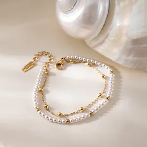 Détail d'un bracelet double couche en acier inoxydable avec perles blanches et dorées.