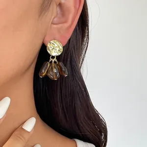 Nahaufnahme von Vintage-Goldohrringen mit braunen Harztropfen an einem Modell