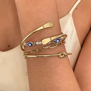 Set di bracciali dorati a strati con perle, ciondoli malocchio e dettaglio a nodo