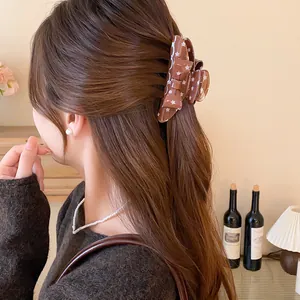 Macro view of a stylish brown bow hair claw clip with white star pattern on model's hair