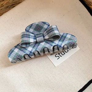 Detail view of a blue and green plaid bow hair claw clip on a beige textured background.
