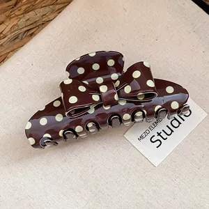 Close-up of retro brown hair claw clip with cream polka dots and an elegant bow detail
