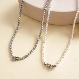 Detail van elegante grijze en witte parelkettingen met geometrische sluitingen met zirkoon.