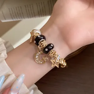 Nahaufnahme eines stilvollen goldfarbenen Armbands mit kristallbesetzten Stern- und Mondanhängern.