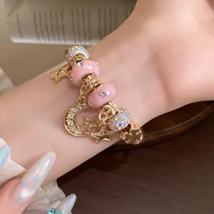 Detailansicht eines Bettelarmbands mit rosa Emaille und goldenen Stern-Mond-Anhängern.