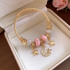 Detailaufnahme eines goldfarbenen Bettelarmbands mit Sternen, Mond und rosa Kristallperlen