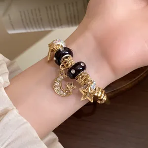 Detailaufnahme eines goldfarbenen Stern- und Mond-Armbands mit schwarzen Perlen.