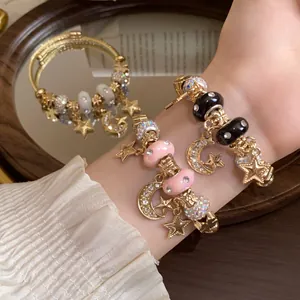 Detailansicht goldener Armbänder mit Stern- und Mondanhängern und Glitzersteinen am Handgelenk