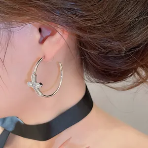 Gros plan de boucles d'oreilles créoles croix argentées avec zircons.