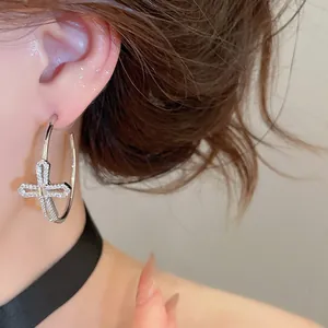Détail rapproché d'une boucle d'oreille créole en argent avec croix en zircon brillant
